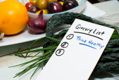 Healthy lifestyle and healthy diet conceptual photography grocery list on kitchen counter with fresh market fruits and vegetables including citrus fruit and superfood kale with chives and tomatoes  handwritten words Grocery List with motivation message for New Years résolution to Think healthy