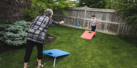 Grandmother and grandson playing corn hole game in a backyard.