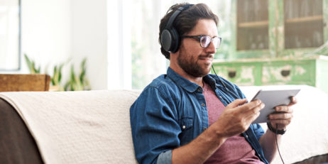 Shot of a man using his tablet and headphones while relaxing on his sofa