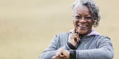 African American senior woman (60s) exercising outdoors, taking pulse.